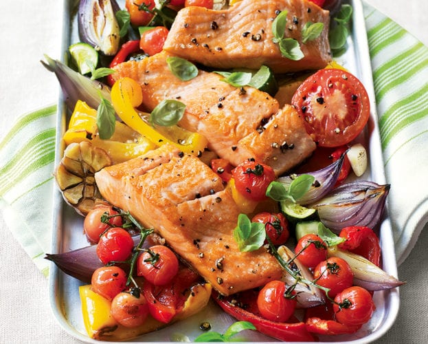 A colourful salmon traybake with peppers, tomatoes and courgettes shown in a silver baking tray