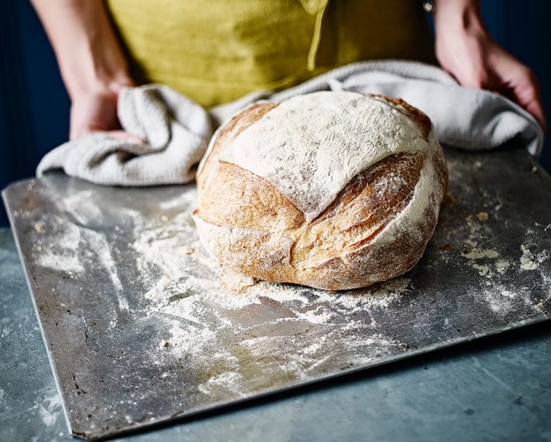 Floury white sourdough loaf on a baking tray