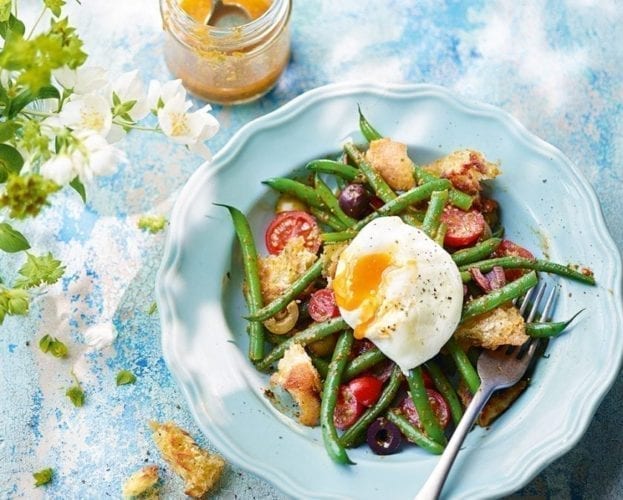 Green beans and tomatoes, with a poached egg on top, shown on a blue plate