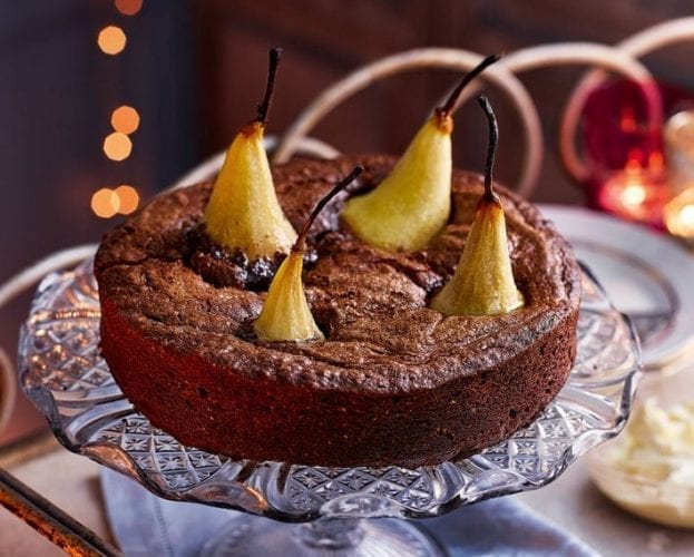 A chocolate cake, decorated with four whole pears, shown on a glass cake stand
