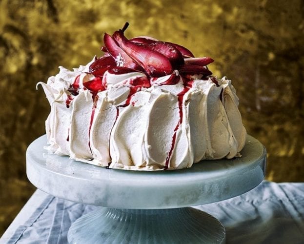 A tall pavlova topped with pears and blackberries, on a marble cake stand