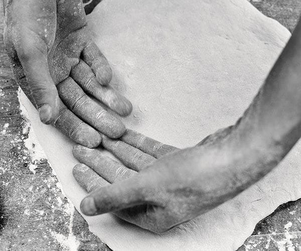 Black and white image of pizza dough and hands