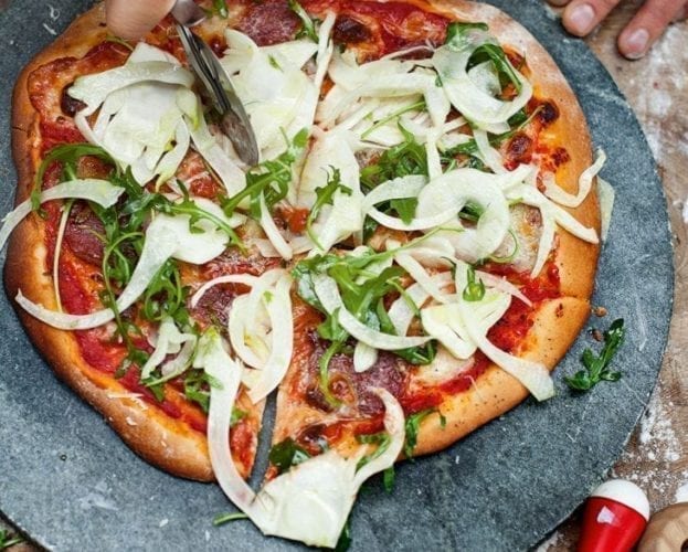 Fennel shown sliced on a pizza on a slate