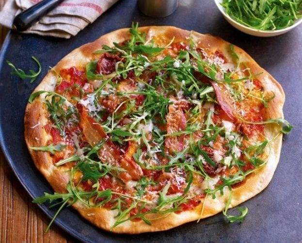 A colourful pizza with pancetta and rocket shown on a pizza plate