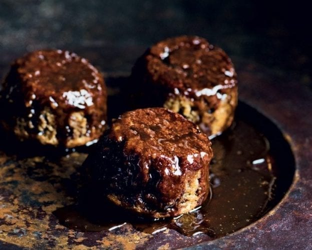 Individual sticky toffee puddings shown on a black plate with a dark moody background