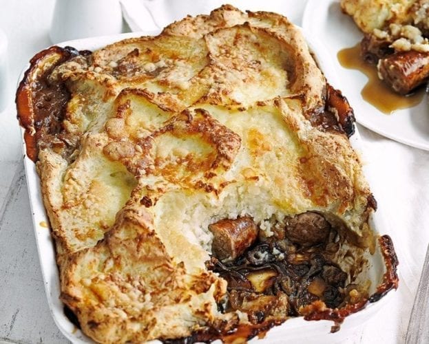 Sausage and mash pie shown in a square dish, with a spoonful taken out