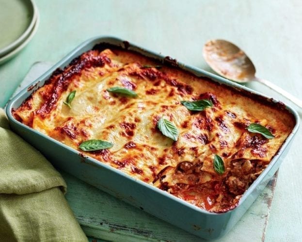 A golden cooked classic lasagne with a large corner scooped out to show the inside