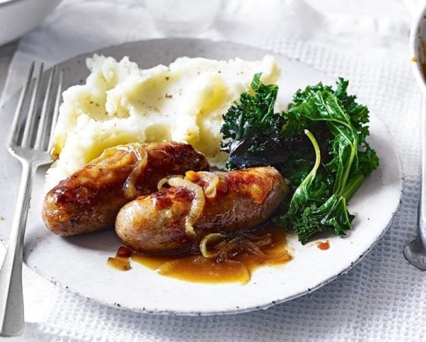 A meal of sausages (covered in onion gravy) and mash on a white plate