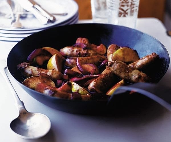 A cooked pan of sausages with apple wedges, shown in a black wide pan