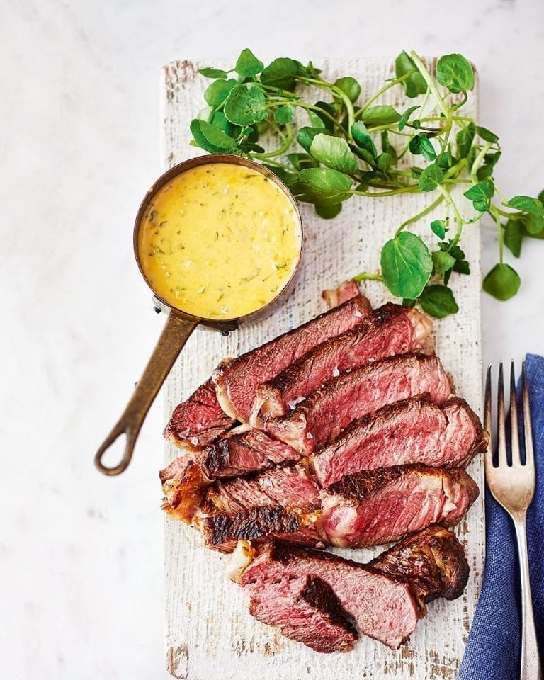 A cooked and sliced steak shown by a small pan of bright yellow bearnaise sauce
