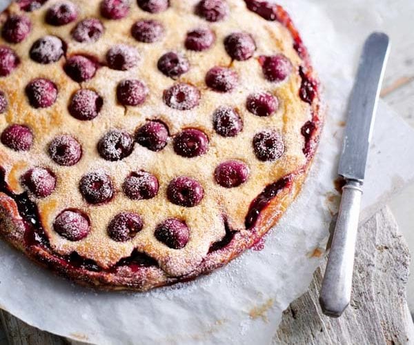 A round cherry bakewell tart, shown cooked and on a piece of greaseproof paper
