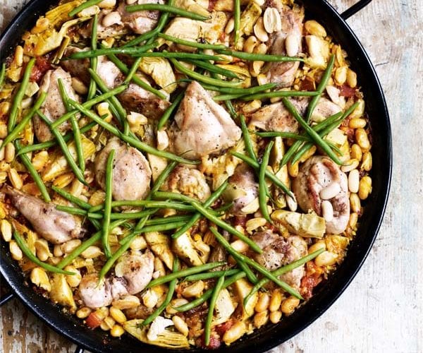 Wild rabbit paella shown in a black paella pan to illustrate a recipe