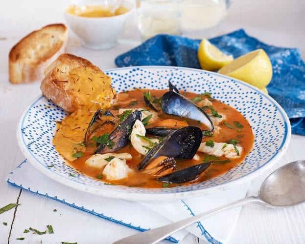 A rich orange-coloured bouillabaisse shown in a blue and white bowl