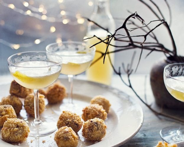 Arancini balls on a plate, shown in a festive setting with fairy lights and cocktails