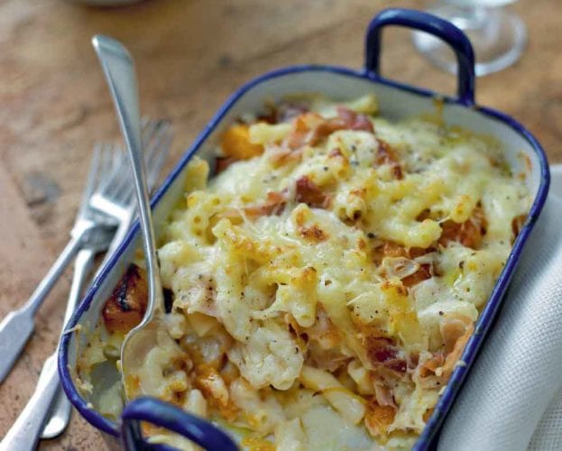 Macaroni cheese in a metal bowl with a scoop of food taken out