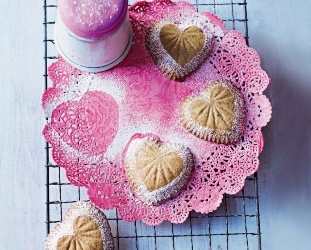 Heart-shaped biscuits covered in icing sugar and shown on a pink plate
