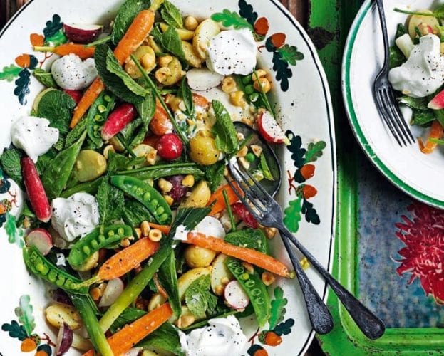 A salad of baby veg and goat's curd shown on an oval plate