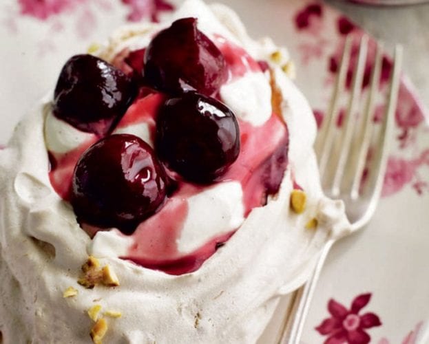 A small individual pavlova with a cherry compote on top, shown on a pretty floral plate