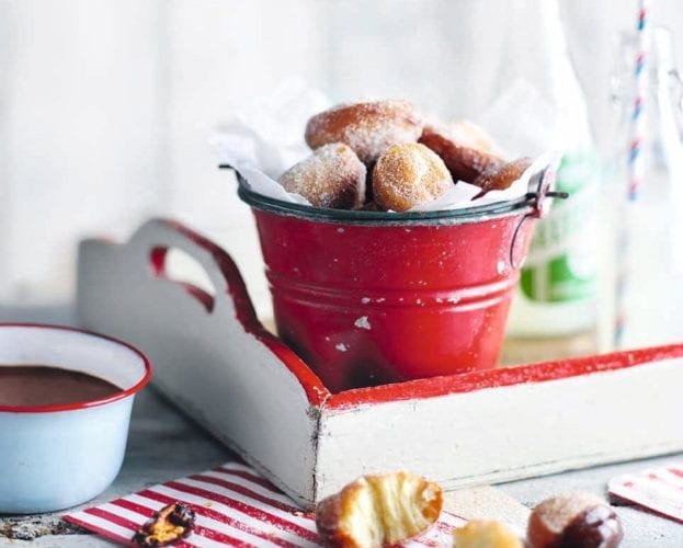 Sugar-dusted cinnamon beignets shown in a little red bucket