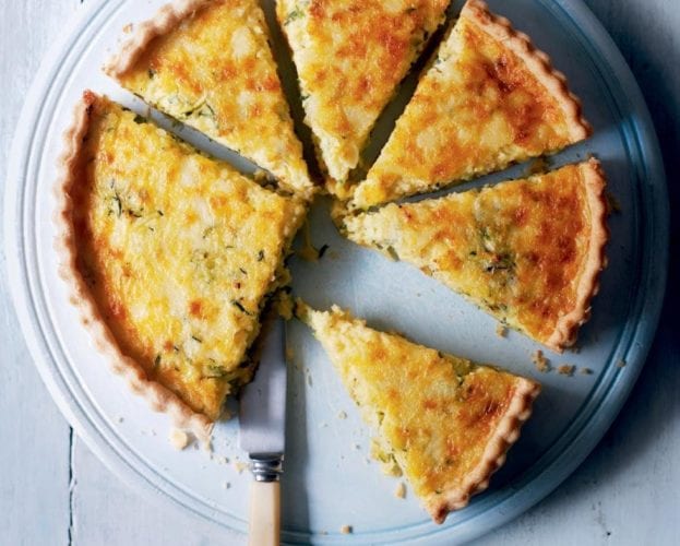 Courgette, onion and cheddar vegetarian tart or quiche, served sliced on a plate