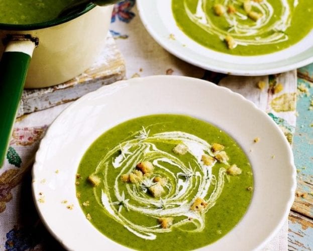 Two bowls of green wild garlic and potato soup topped with swirls of double cream and golden croutons