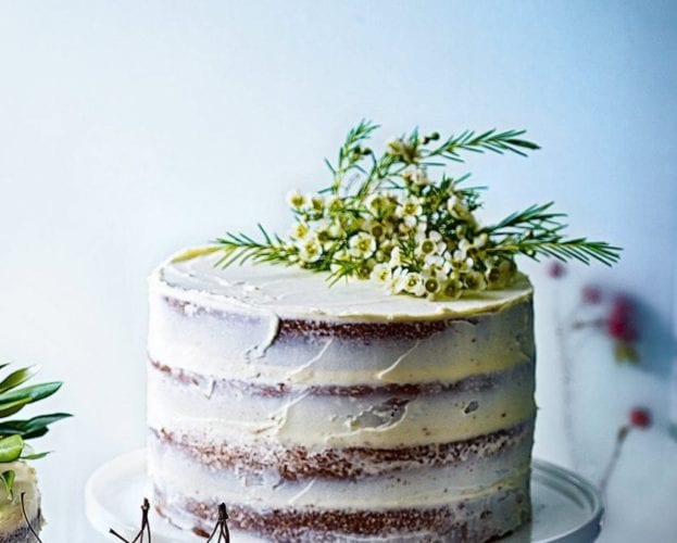 A tall four layer naked cake, with buttercream icing and a floral decoration