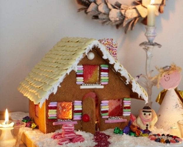 A decorated gingerbread house surrounded by candles and decorations