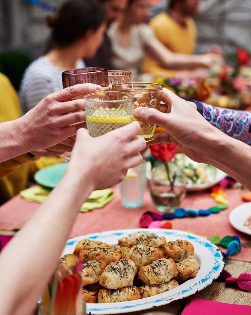 Image of people clinking glasses over a plate of sausage rolls