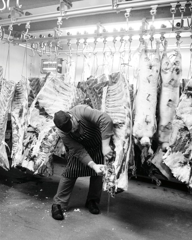 black and white image of a butcher removing meat from a carcass 