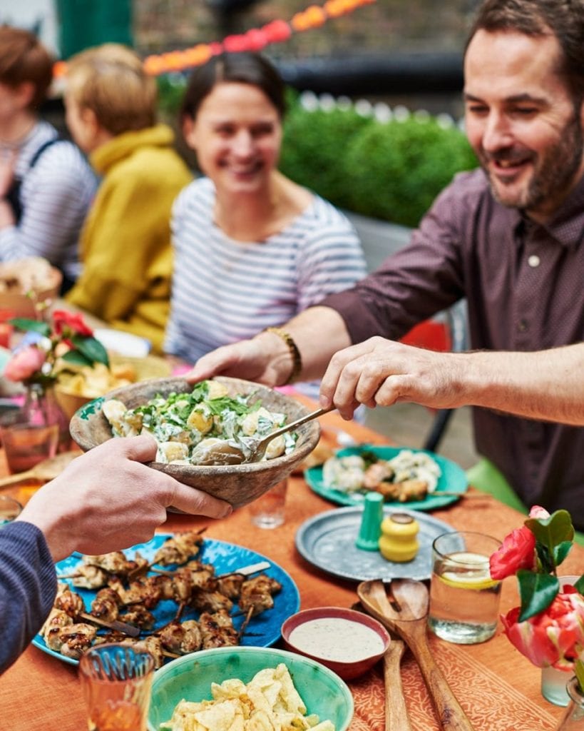 Image of a man passing a bowl of potato salad to another guest