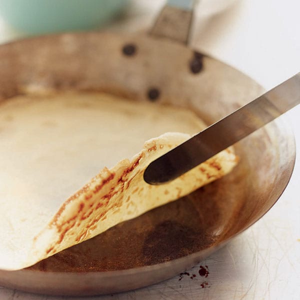 A corner of a cooked pancake in a pan being lifted by a palette knife