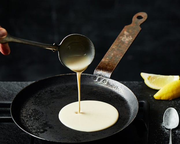 A ladle of pancake batter being poured into a pan