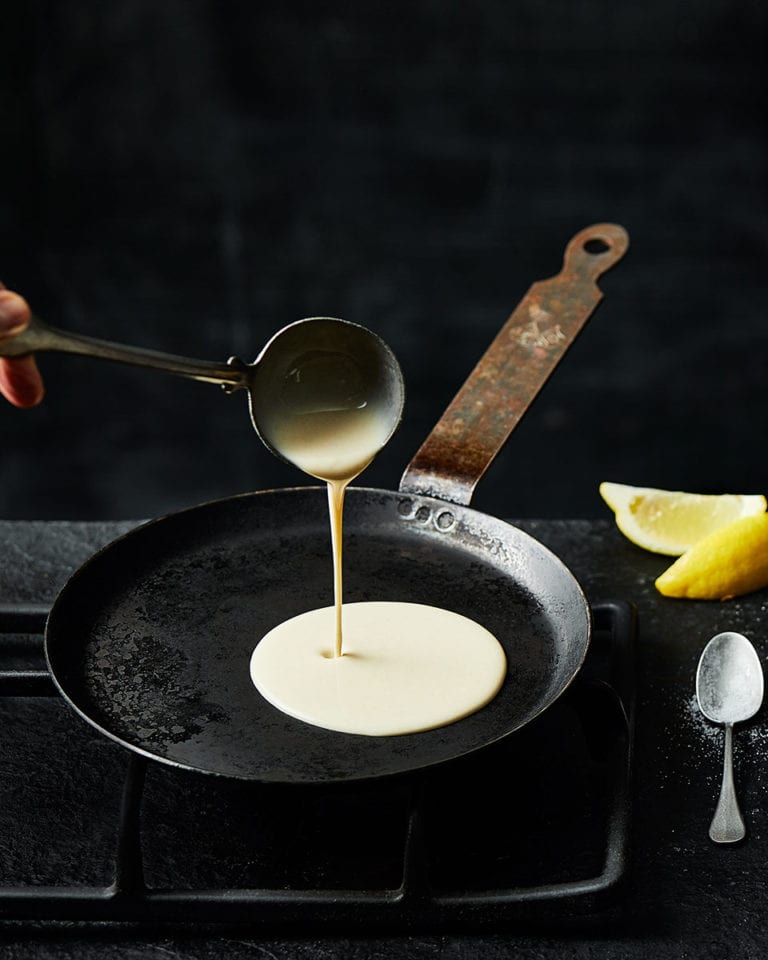 A ladle of pancake batter being poured into a pan