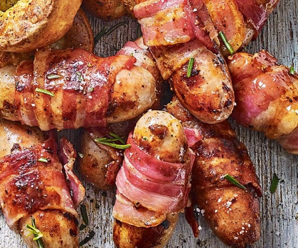 Pigs in blankets (sausages wrapped in bacon) shown on a wooden board