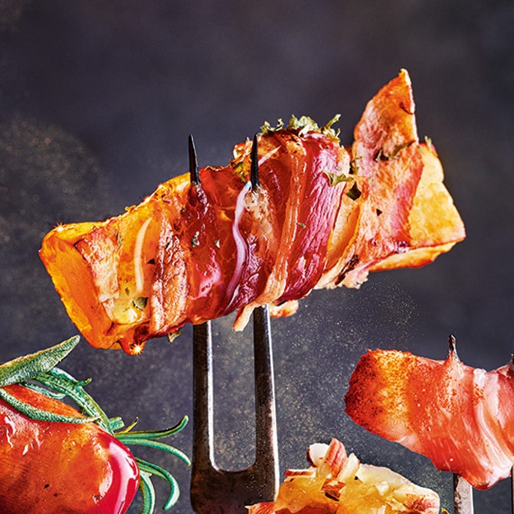 A strip of halloumi wrapped in bacon speared on a fork