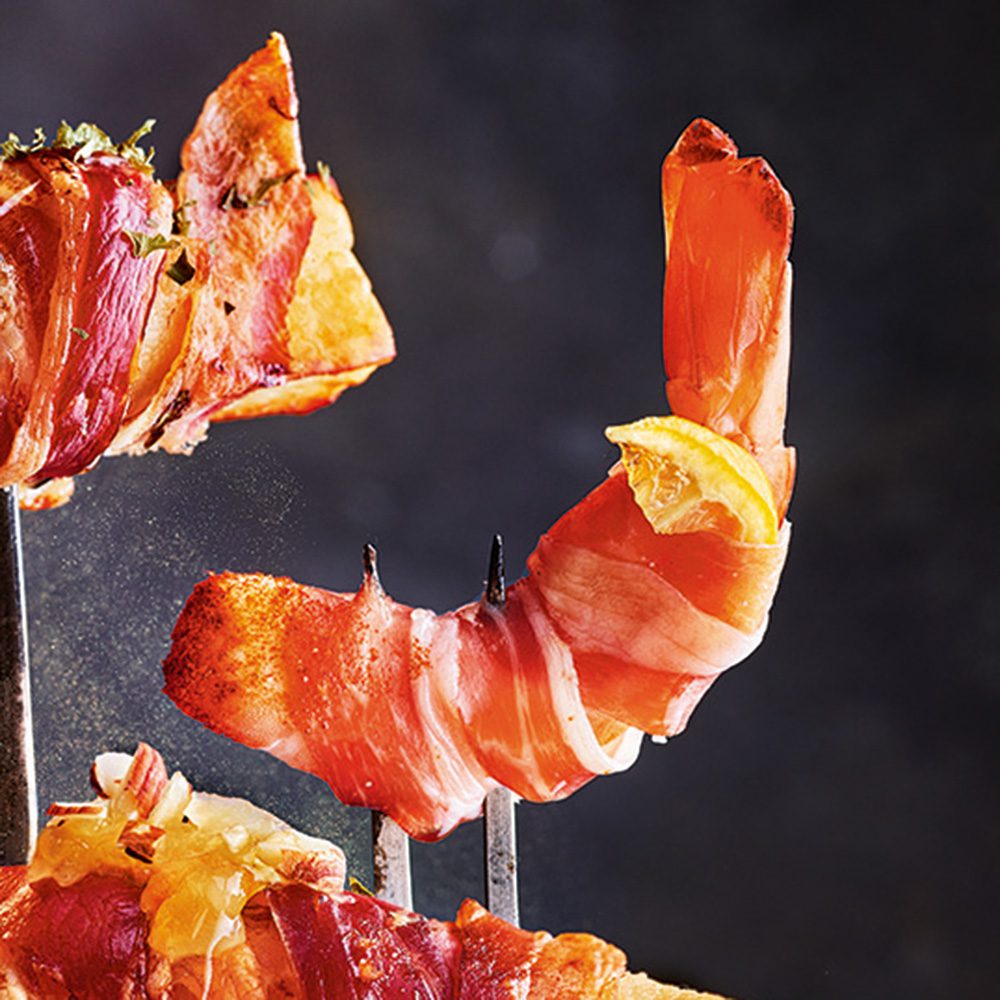 A prawn wrapped in bacon speared on a fork