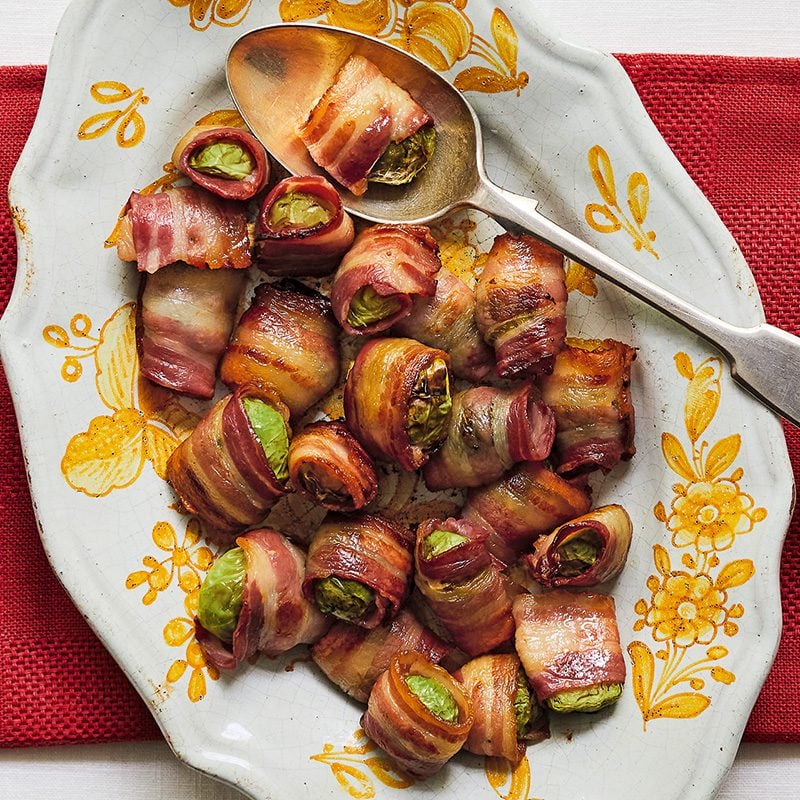 Sprouts wrapped in bacon on an ornate platter with a spoon