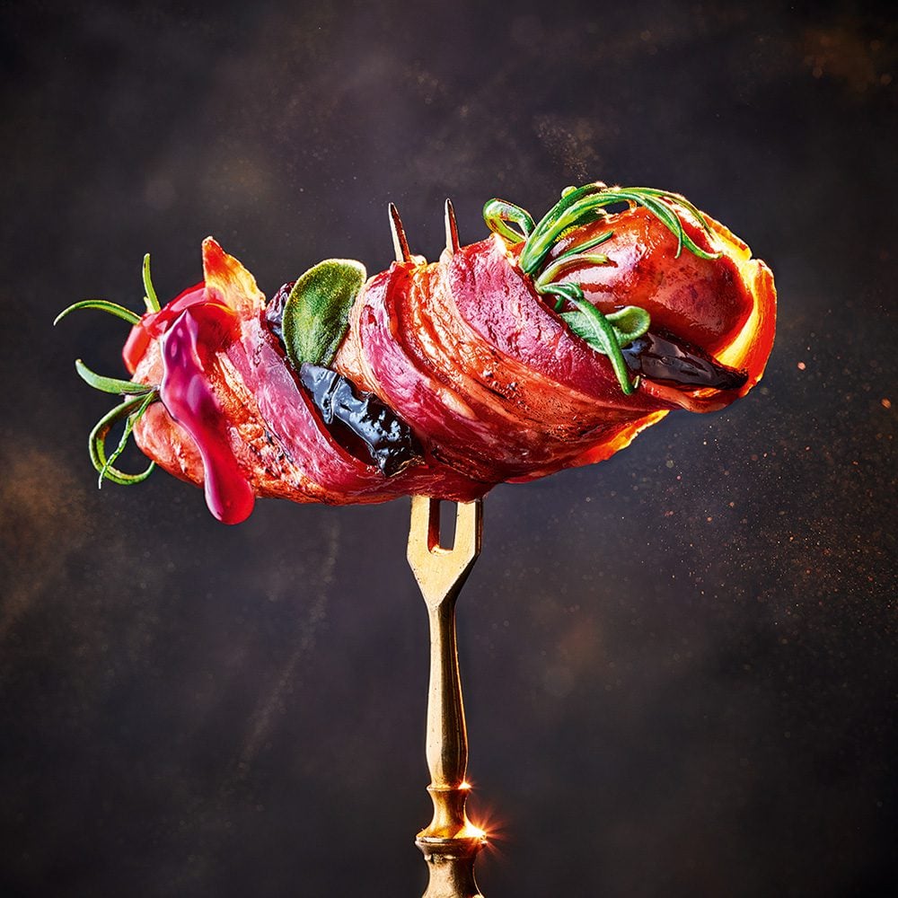 A pig in blanket garnished with herbs and speared on a fork