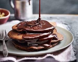 Chocolate pancakes with a drizzle of chocolate being poured over them