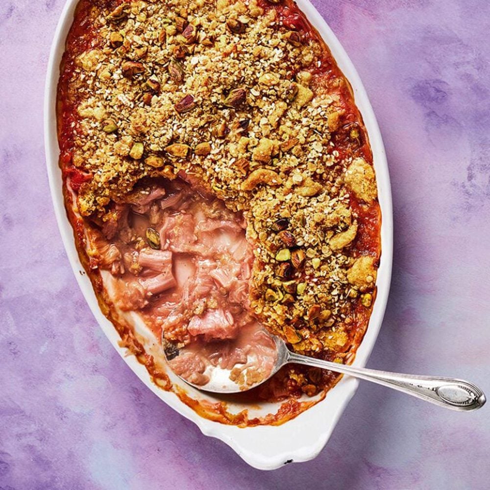 An overhead view of rhubarb crumble in an oval dish, with serving spoon