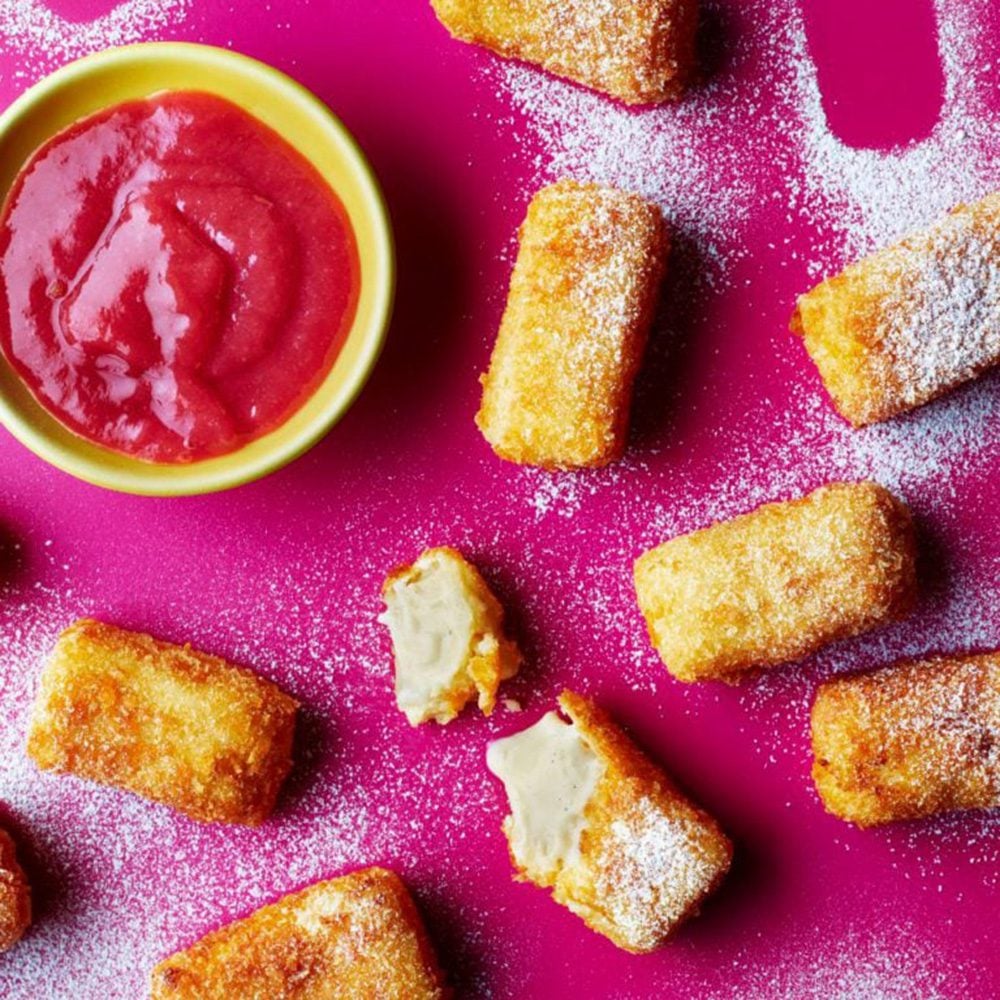 An overhead view of deep-fried custard cubes with rhubarb dipping sauce in a yellow dish