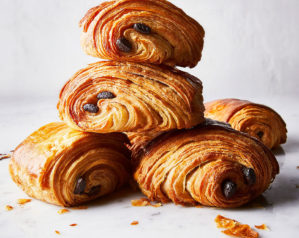 Five cooked, flaky pain au chocolat are shown in pile on a white background