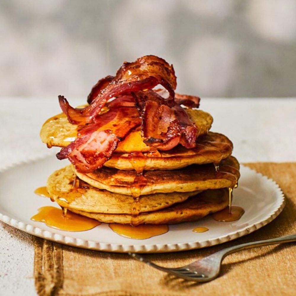 A stack of pancakes topped with crispy bacon and maple syrup