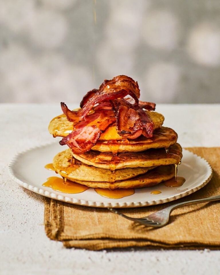 A stack of pancakes topped with crispy bacon and maple syrup