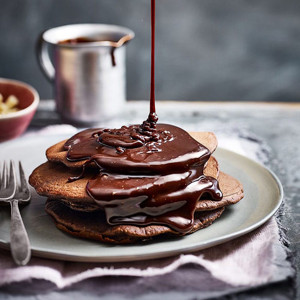 A stack of chocolate pancakes being drizzled with chocolate sauce