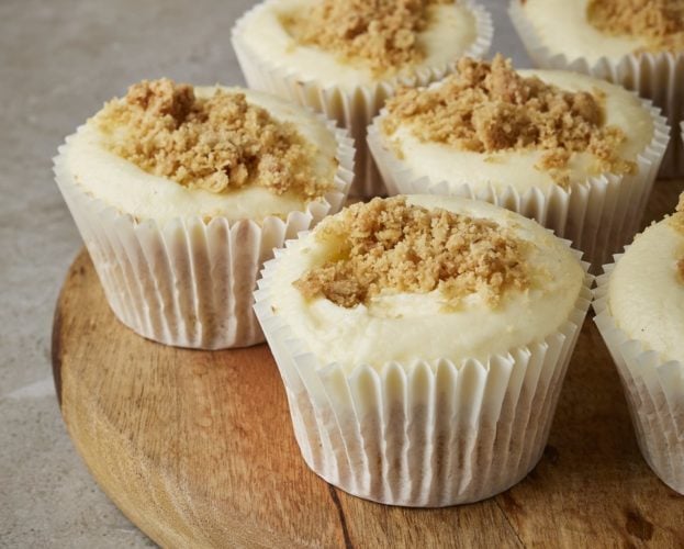 Apple crumble cupcakes shown in white cases on a wooden tray