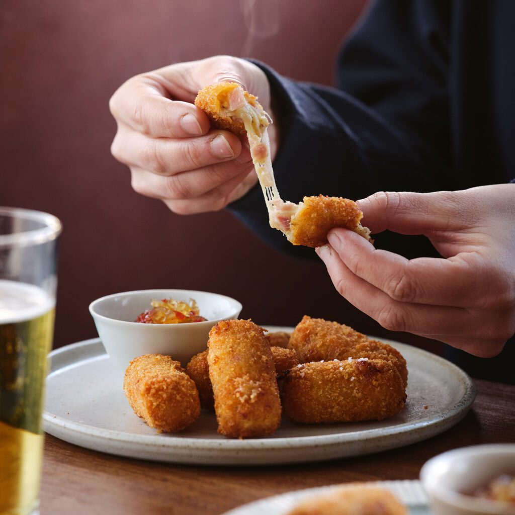 A plate of cheesy croquettes with one being pulled apart