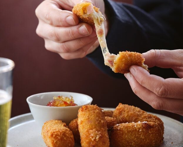 A plate of cheese and ham croquettes with one being pulled apart