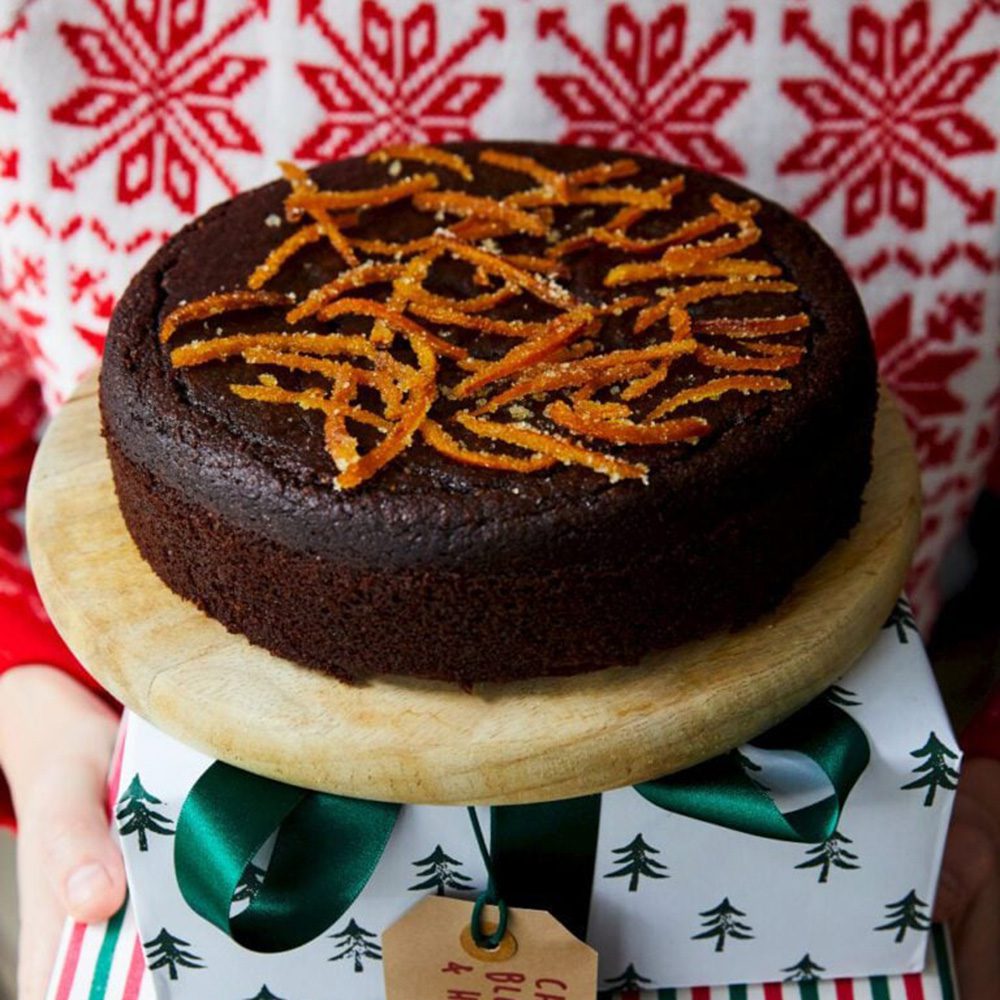 A chocolate cake topped with candied orange zest on a wooden board