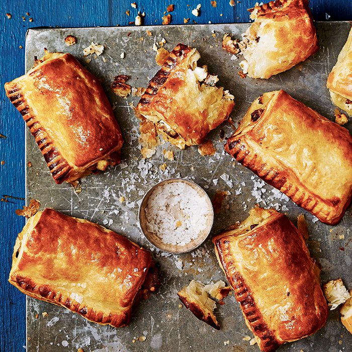 Golden filo sausage rolls on a board, sprinkled with flaky salt